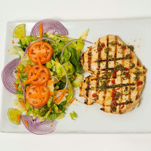 Grilled chicken breast with chimichurri sauce, served with a fresh garden salad and lime wedges.