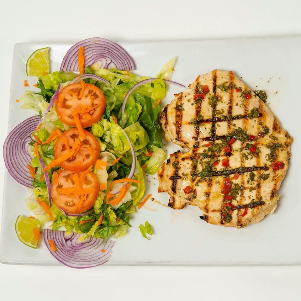 Grilled chicken breast with chimichurri sauce, served with a fresh garden salad and lime wedges.