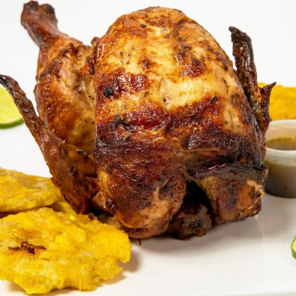 Whole grilled chicken with crispy skin, served with fried plantains and a side of sauce.