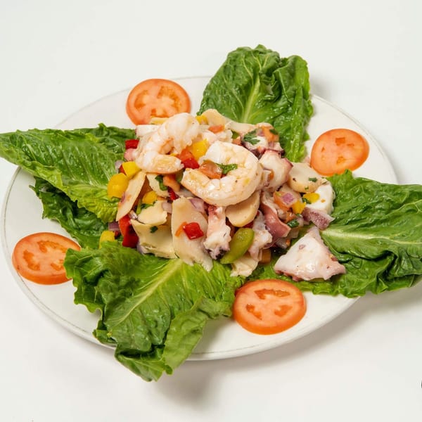 Seafood ceviche with shrimp, octopus, and vegetables on a bed of lettuce with tomato slices.