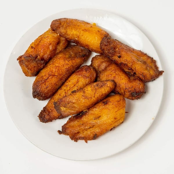 A white plate holds several golden-brown, crispy fried plantains, a side dish from Pollo Lounge and Grill.