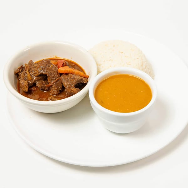 Beef stew with carrots and peppers, a side of rice, and a bowl of orange sauce.