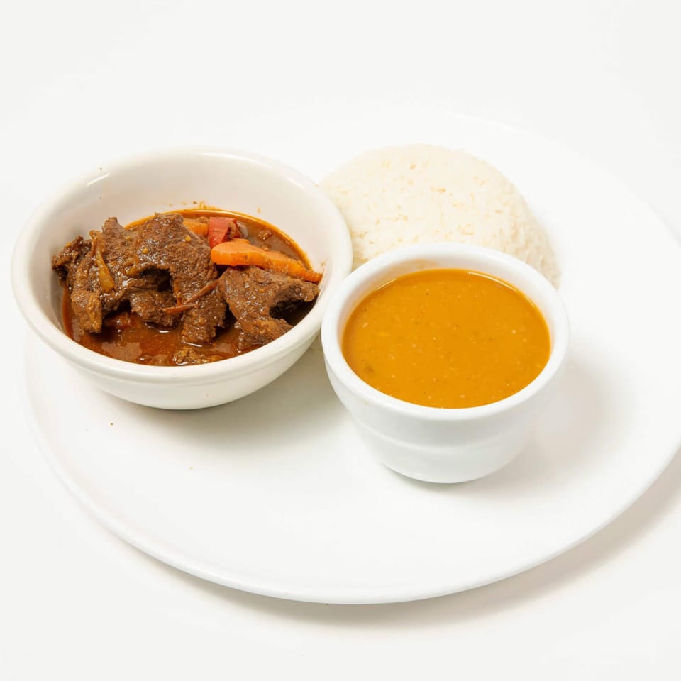 Beef stew with carrots and peppers, a side of rice, and a bowl of orange sauce.